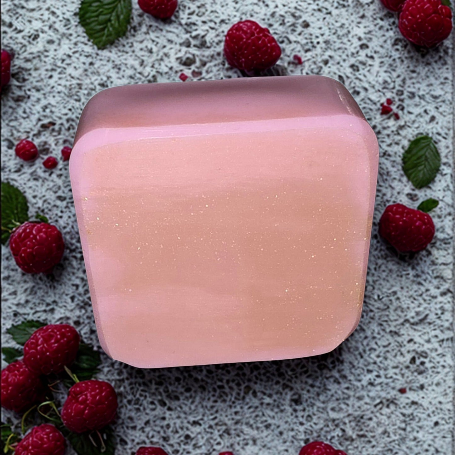 Pink soap bar on a textured surface with raspberries and leaves