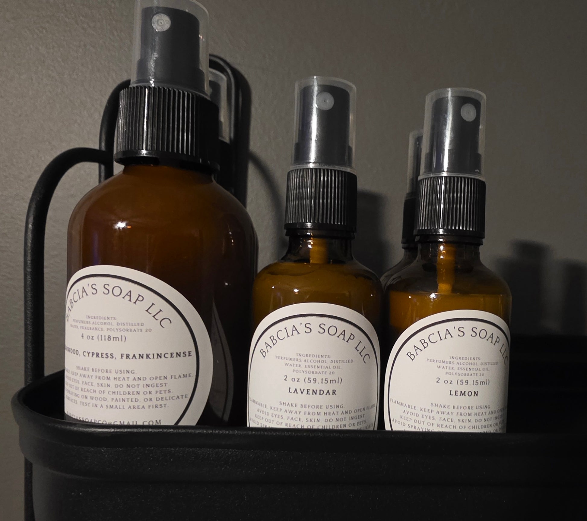 Three bottles of Babcia's Soap LLC products on a dark surface with a gray background.