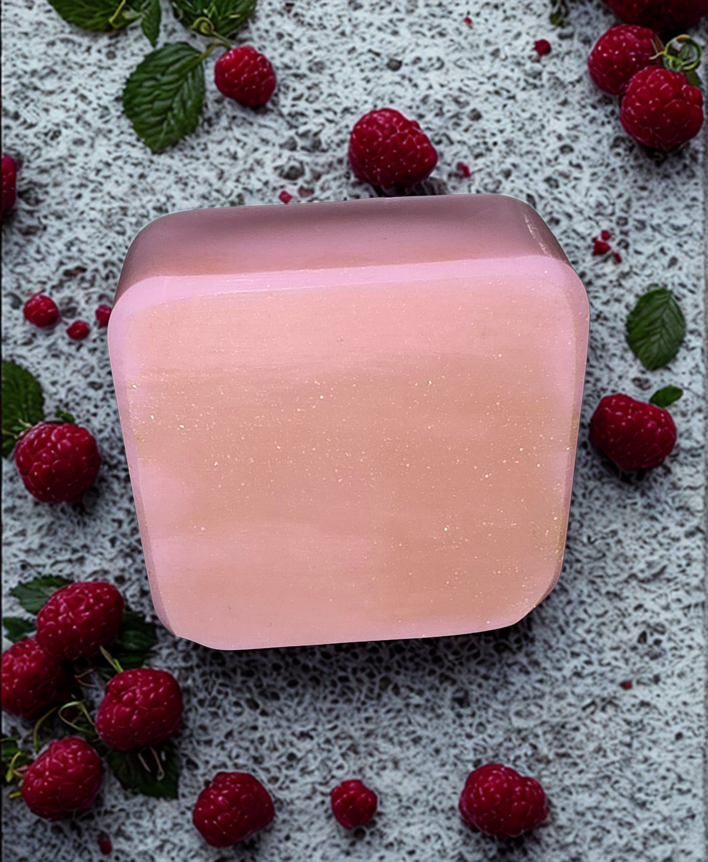 Pink soap bar on a textured surface with raspberries and leaves