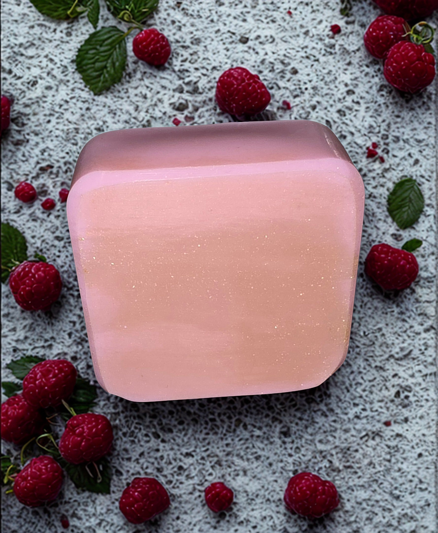 Pink soap bar on a textured surface with raspberries and leaves