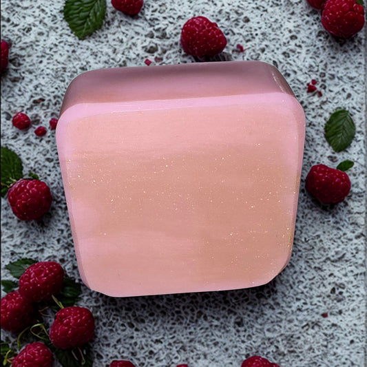 Pink soap bar on a textured surface with raspberries and leaves
